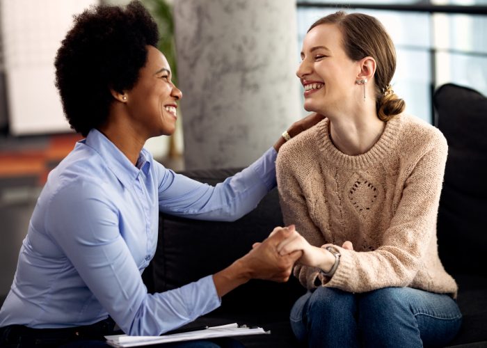 Young happy woman holding hands with her psychotherapist during an appointment at the clinic.