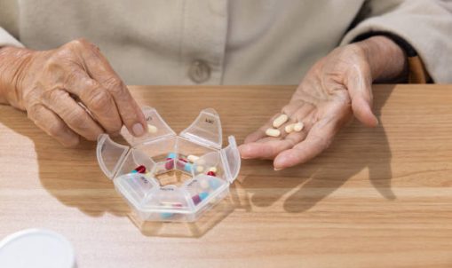 Elderly woman putting pills into pill box for the week.
